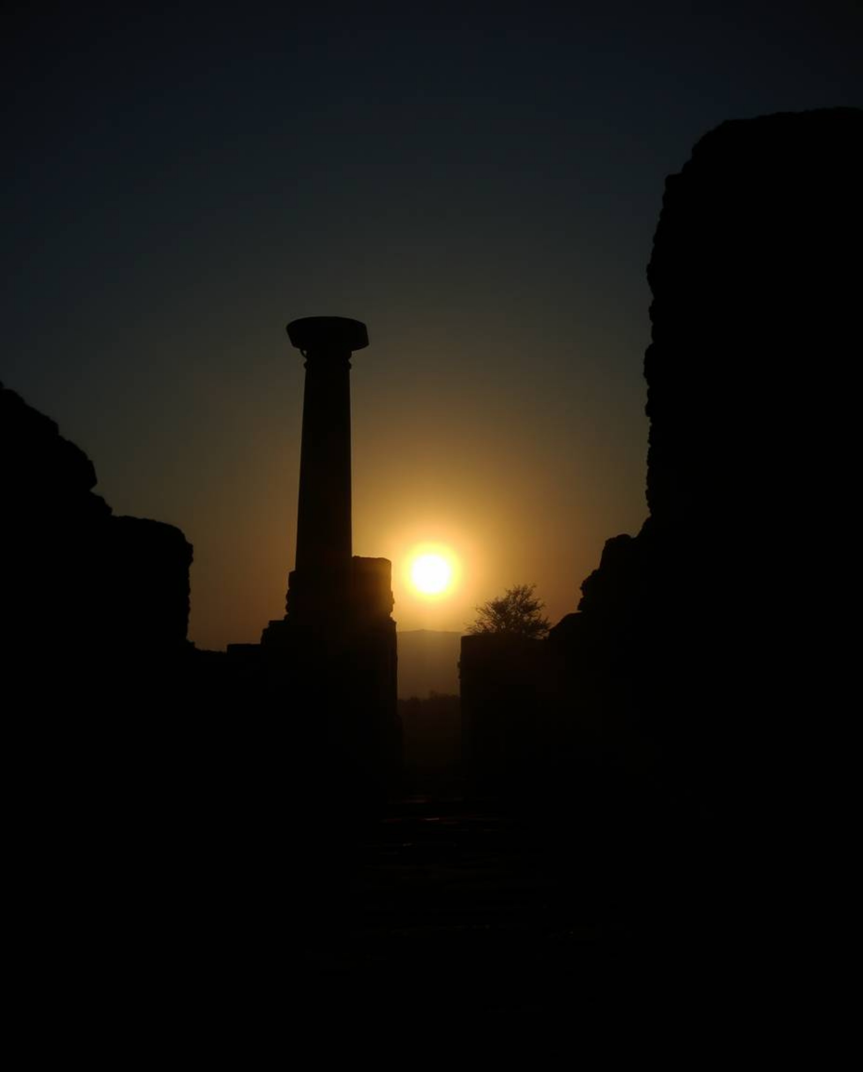 A high-contrast, low-key cinematic style image depicts a sunset casting shadows through ancient stone ruins. This piece empha