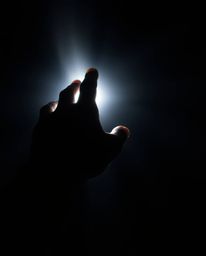 A captivating image of a hand reaching towards a light source, emerging from deep shadows.  High contrast and a high-angle sh