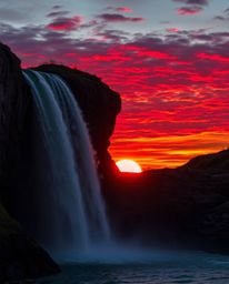 A warm sunset in reds, oranges, and yellows behind a dramatic waterfall, showcasing vibrant colors and a naturally lit atmosp