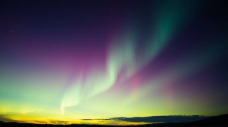 Experience the awe-inspiring beauty of the Northern Lights dancing across a vibrant sunset sky in this dramatic, cinematic im