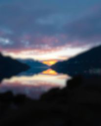 This artwork portrays the reflection of a sunset in a glassy fjord, rendered in a modern flat design style. The composition f