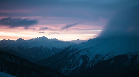 Experience the unsettling beauty of snow-covered mountains glowing under a pastel sunset. This image evokes a creepy, eerie a