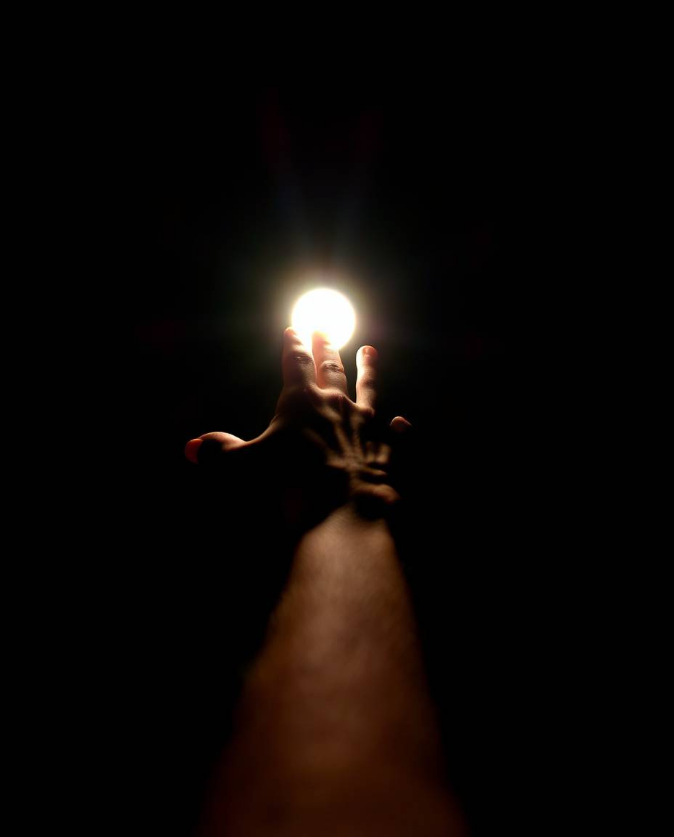 This image captures a hand reaching towards a bright light emanating from darkness, creating a powerful visual metaphor. The 