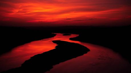 A dramatic scene unfolds with warm, contrasting chiaroscuro lighting highlighting a winding river glowing under a vibrant ora