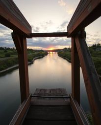 Captured from a high-angle perspective, an old wooden bridge stretches over a river at sunset. This elevated viewpoint, looki