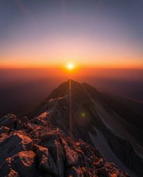 This is a long exposure photograph of a high-alpine peak sunset, characterized by a bright lens flare and captivating light s