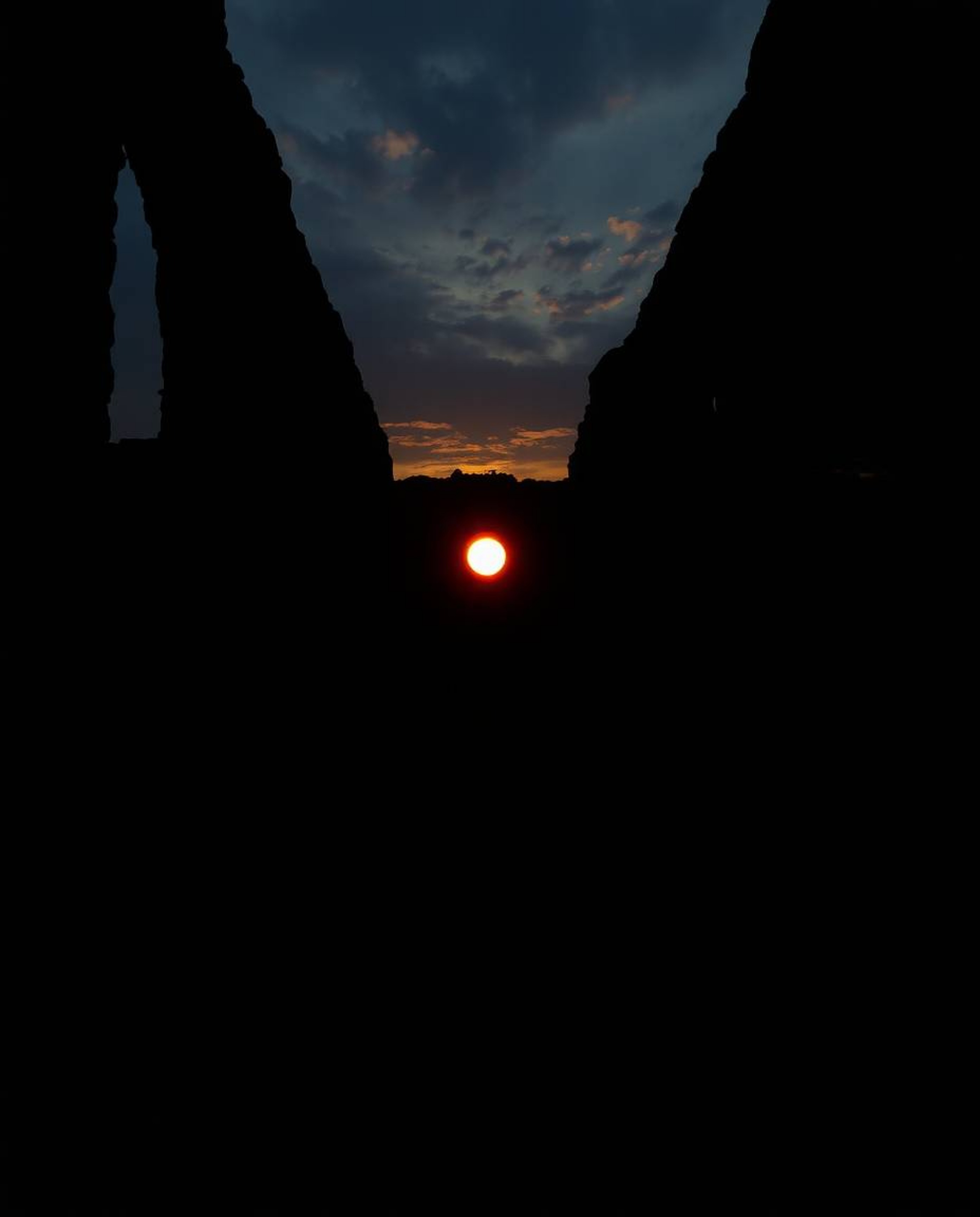 An eerie sunset casts long shadows through ancient stone ruins, creating a creepy, mystic atmosphere. The scene is characteri