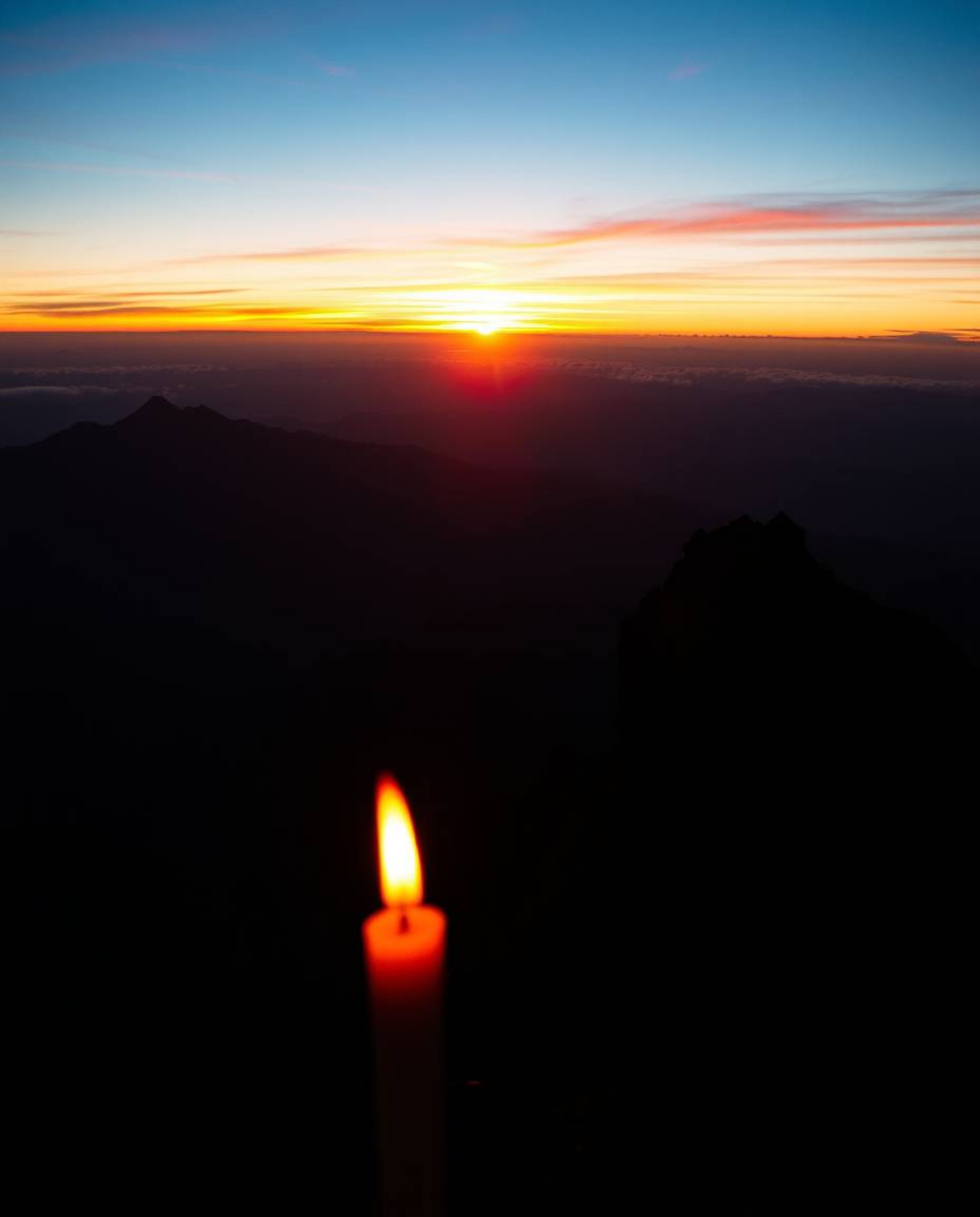 This is a dramatic cinematic-style image of a sunset viewed from a high alpine peak. The scene is uniquely illuminated by the