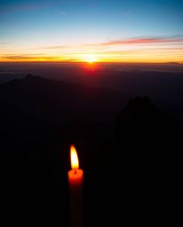This is a dramatic cinematic-style image of a sunset viewed from a high alpine peak. The scene is uniquely illuminated by the