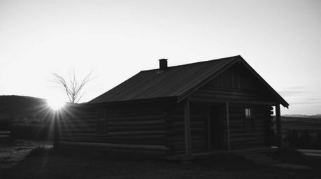 A timeless black and white photograph captures an old wooden cabin bathed in the soft, golden light of sunset.  The elegant a
