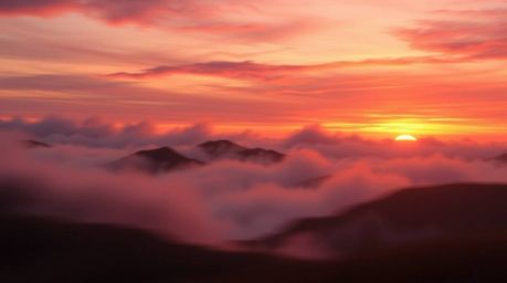 A stunning digital painting depicting fog-covered hills bathed in the warm, dynamic light of a sunset.  The artwork features 