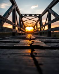 This is a close-up shot of an old wooden bridge at sunset, highlighting its distinct split cast bronze surface. The image fea