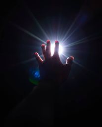 A captivating photograph depicting a hand reaching towards a source of radiant light emerging from darkness. The image is enh