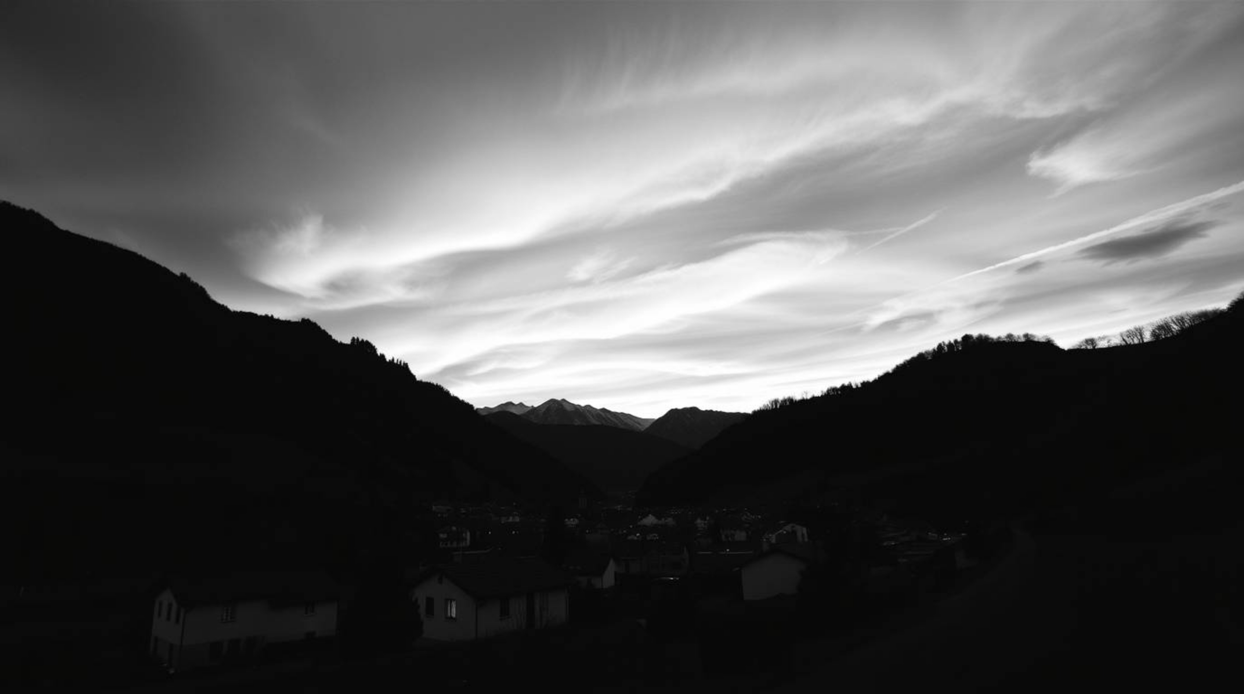 A captivating classic black and white photograph showcases a cozy village nestled peacefully in a valley, set against the bac