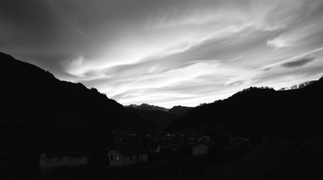 A captivating classic black and white photograph showcases a cozy village nestled peacefully in a valley, set against the bac