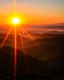 A vibrant sunset over misty Tuscan hills, split into distinct sections with a bright lens flare, bold light streaks and satur