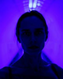 A dramatic cinematic image captures a person with pale skin and intense eyes standing at the edge of a tunnel, bathed in deep