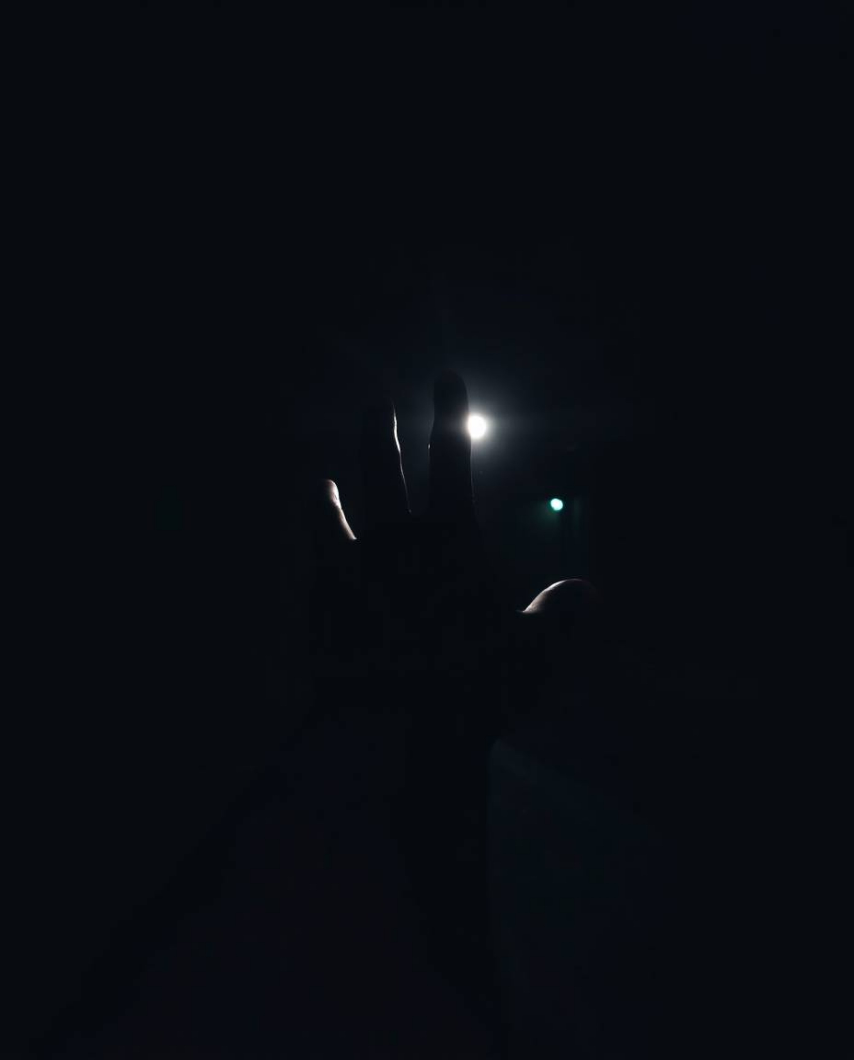 This candid, moody, low-contrast street photograph captures a hand reaching towards a source of light emerging from darkness,