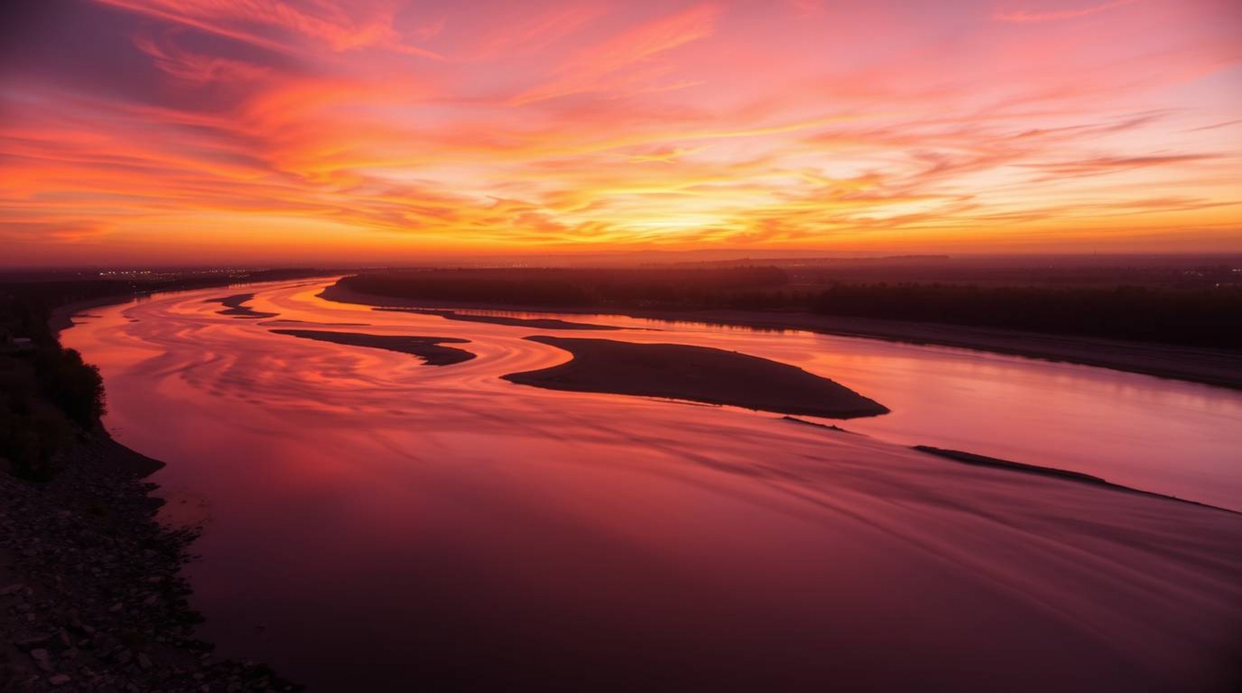 Capture the serene beauty of a winding river illuminated by a dramatic orange-pink sunset in this long-exposure photograph. U