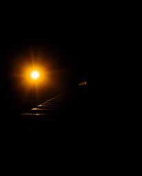 This is a chiaroscuro-lit photograph capturing an old wooden bridge at sunset. The image features a sharp focus on the bridge