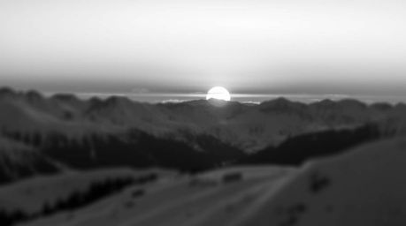 A timeless and elegant black and white photograph showcasing snow-covered mountains bathed in the soft glow of a pastel sunse