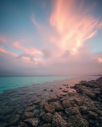 A photograph captures a colorful sky over a coral reef at low tide, distinguished by its soft cinematic haze and gentle soft 