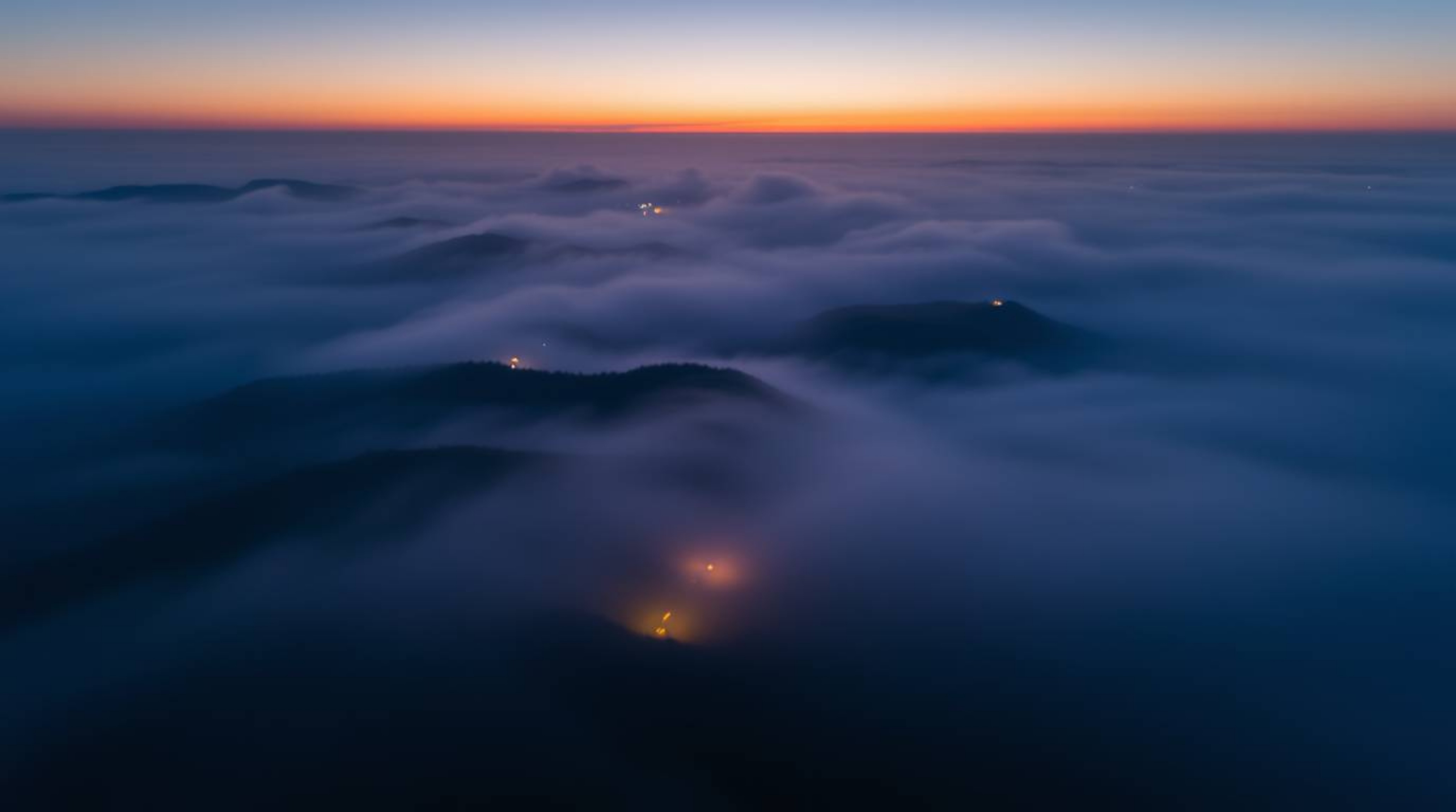 This breathtaking long exposure photograph captures a bird's eye view of fog-covered hills bathed in the warm light of the se