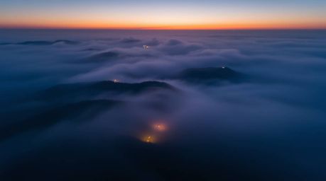 This breathtaking long exposure photograph captures a bird's eye view of fog-covered hills bathed in the warm light of the se