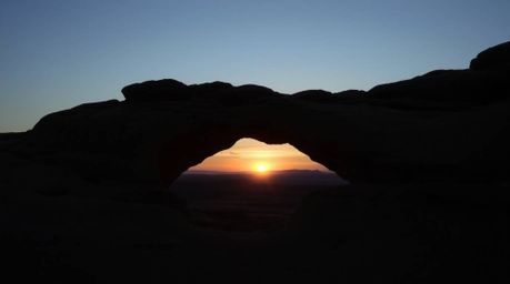 A captivating fine art photograph captures a serene sunset viewed through a natural desert rock arch.  The image boasts soft,