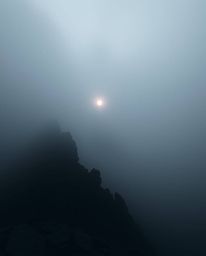 Experience an eerie and creepy atmosphere where a thick fog almost completely obscures a sunset viewed from a high alpine pea