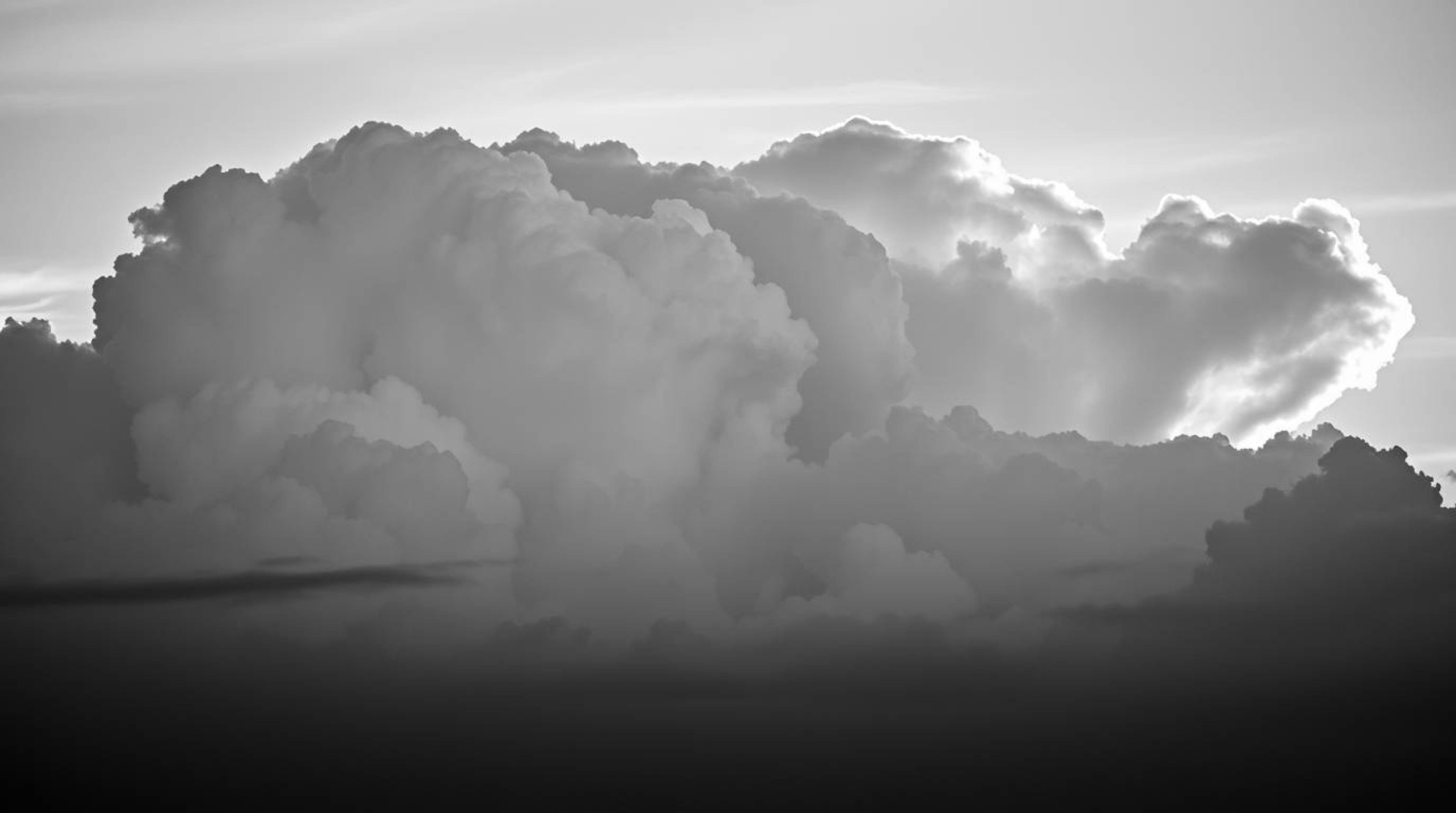A timeless and elegant black and white photograph captures the dramatic beauty of thunderstorm clouds illuminated by the warm