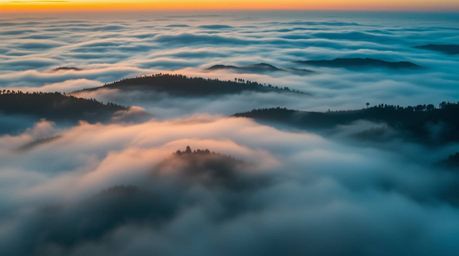 A stunning bird's-eye view photograph captures luxurious and vibrant fog-covered hills bathed in the rich, deep teal hues of 