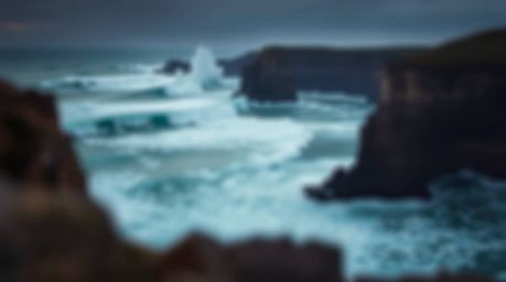 A stunning photograph captures waves crashing dramatically against cliffs during a blazing sunset, creating a moody atmospher