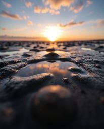 An extreme macro close-up photograph captures the intricate details of a sunset sky as it is mirrored in the tidal pools on a