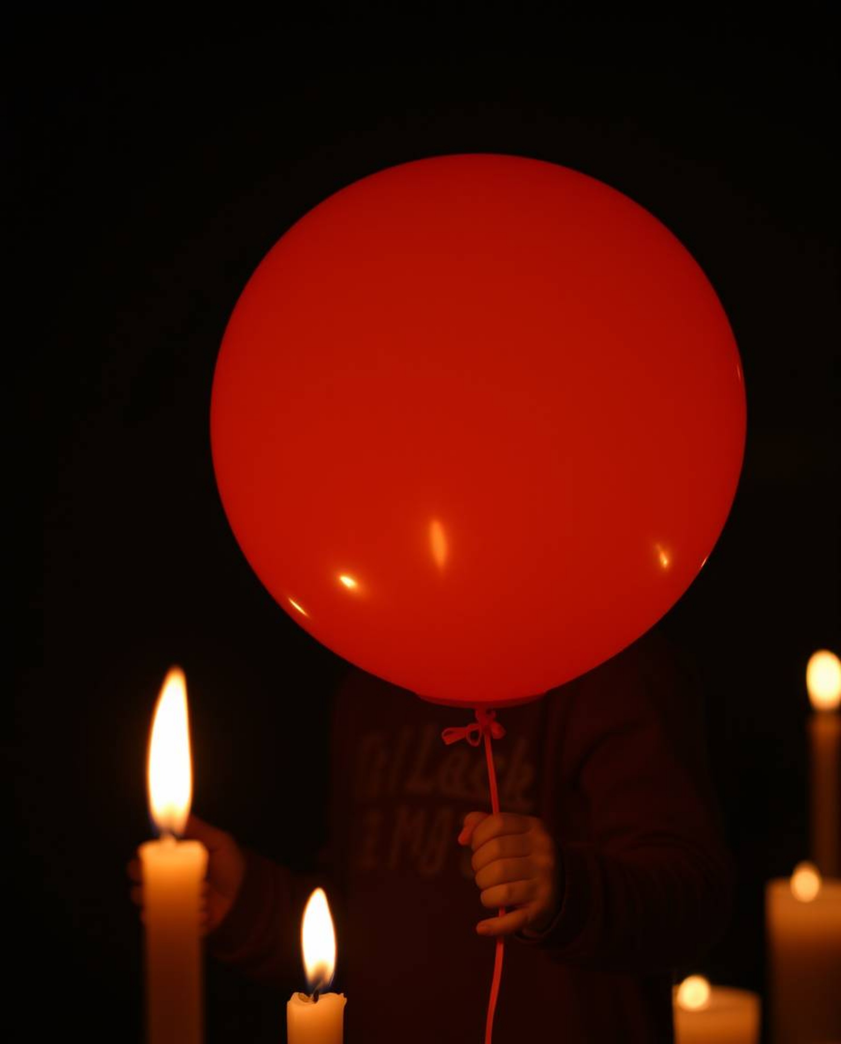 A captivating image of a child gently holding a balloon in the warm, flickering light of candles. The scene is bathed in pred