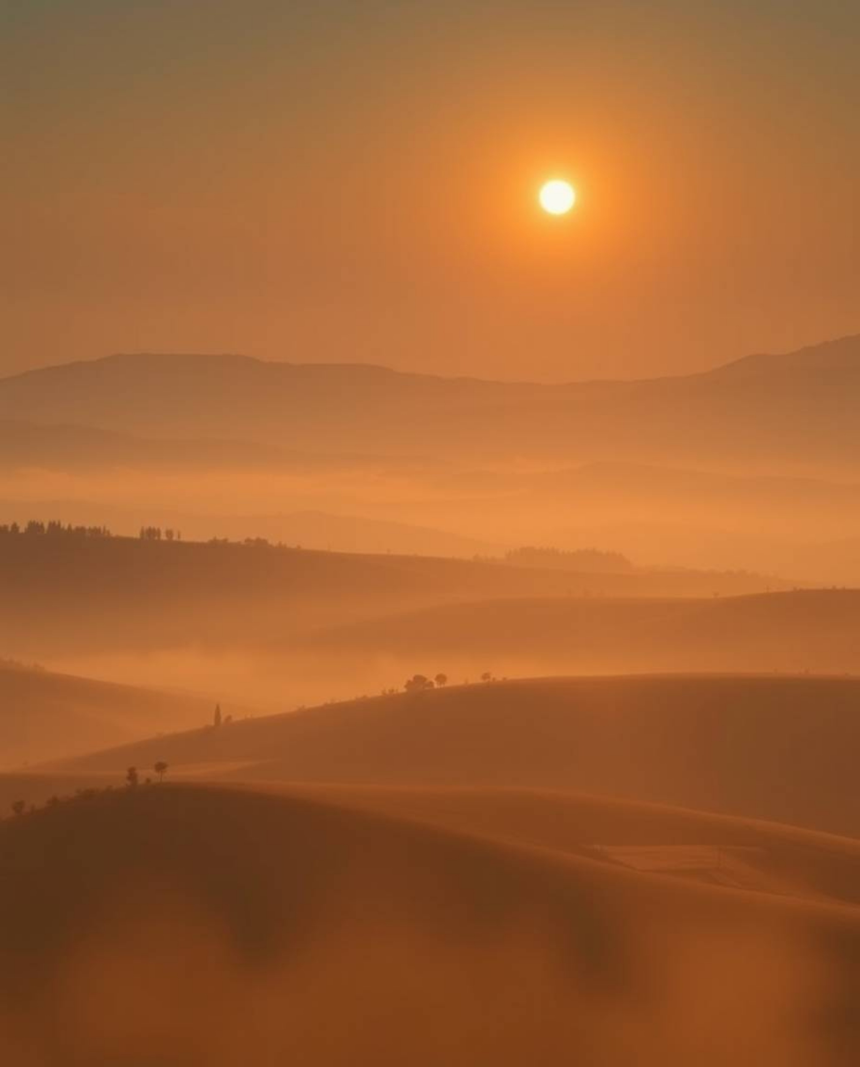 This image provides a high-angle perspective view of a sunset over the misty, rolling hills of Tuscany. Characterized by a so