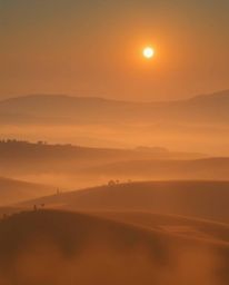 This image provides a high-angle perspective view of a sunset over the misty, rolling hills of Tuscany. Characterized by a so