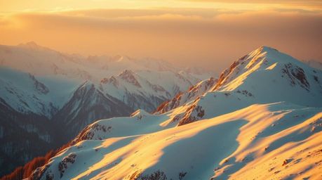 Experience the serene beauty of snow-covered mountains illuminated by the warm glow of the golden hour or bathed in the soft 
