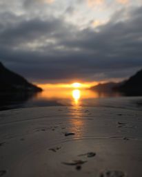 A cast bronze surface depicts the reflection of a sunset in a glassy fjord, characterized by contrasting chiaroscuro lighting