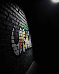 Capture the dynamic energy of vibrant graffiti splashed across a textured brick wall, dramatically lit with chiaroscuro techn