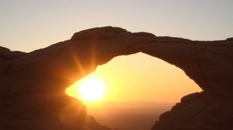 Capture the soft and dreamy essence of a desert sunset framed by a natural rock arch. This image features hazy light, diffuse