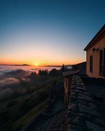This is a precise architectural photograph of a sunset over the misty, rolling hills of Tuscany. The image is characterized b