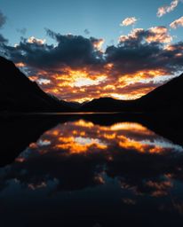 Captured from a high-angle perspective, this image shows the reflections of fiery clouds in a mountain lake, viewed while loo