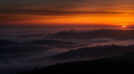 A moody and dramatic image capturing fog-covered hills at sunset. The high-contrast and intense lighting create a sense of te