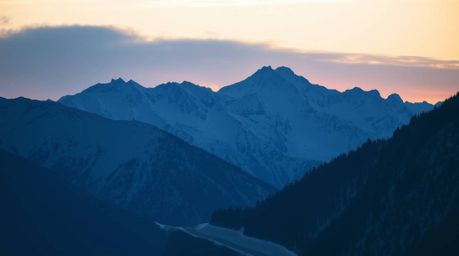 Experience the serene beauty of snow-covered mountains silhouetted against a pastel sunset, bathed in cool blues, greens, and