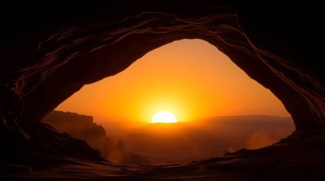 A breathtaking desert sunset is dramatically captured through a natural rock arch.  Rendered in intense jet black and white, 