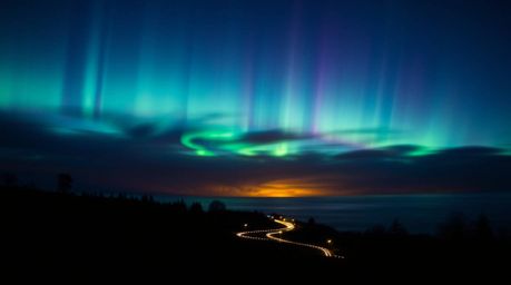 Witness the breathtaking spectacle of the Northern Lights dancing across a vibrant sunset sky in this dramatic long exposure 