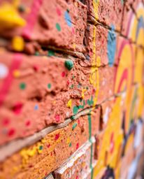 An extreme macro close-up reveals the intricate details and vibrant colors of graffiti-style splashes on a brick wall. This c