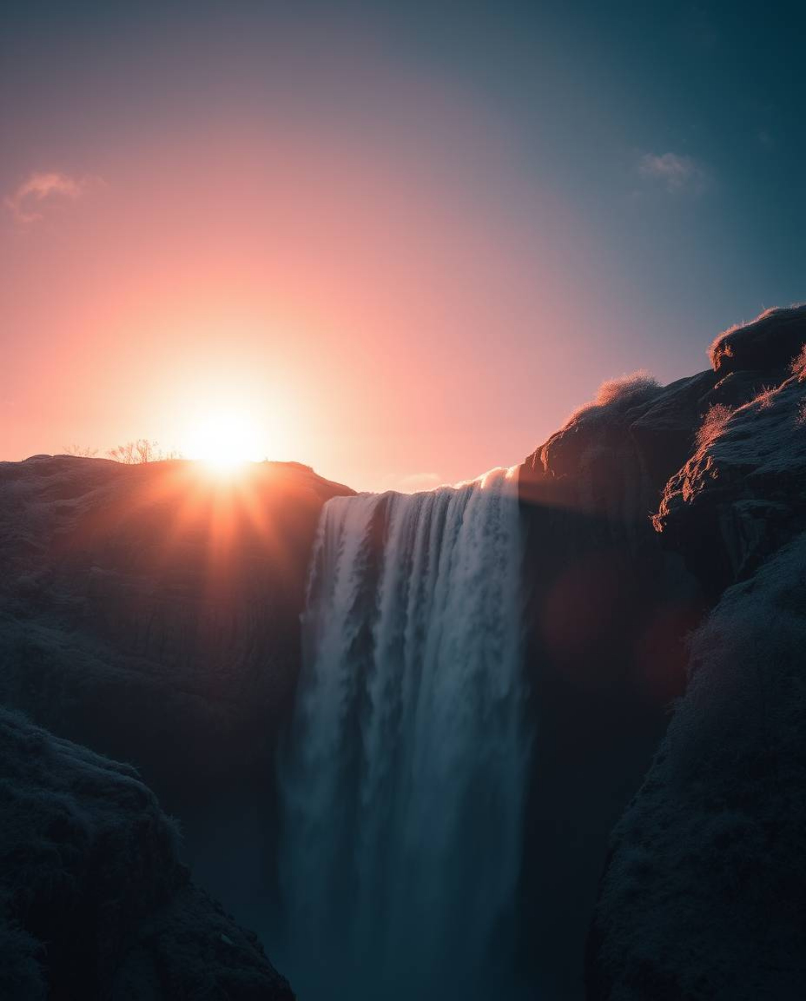 A surreal image of a sun setting behind a dramatic waterfall, using infrared tones and chiaroscuro lighting. This combination