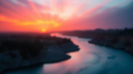 A stunning landscape featuring a winding river bathed in the ethereal glow of a dramatic orange-pink sunset sky. Volumetric l
